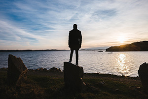 The Starting Point and Foundation of a Proper Worldview - Weekly Blog Post by Dr. Craig Biehl - man standing on rock by water's edge at sunset